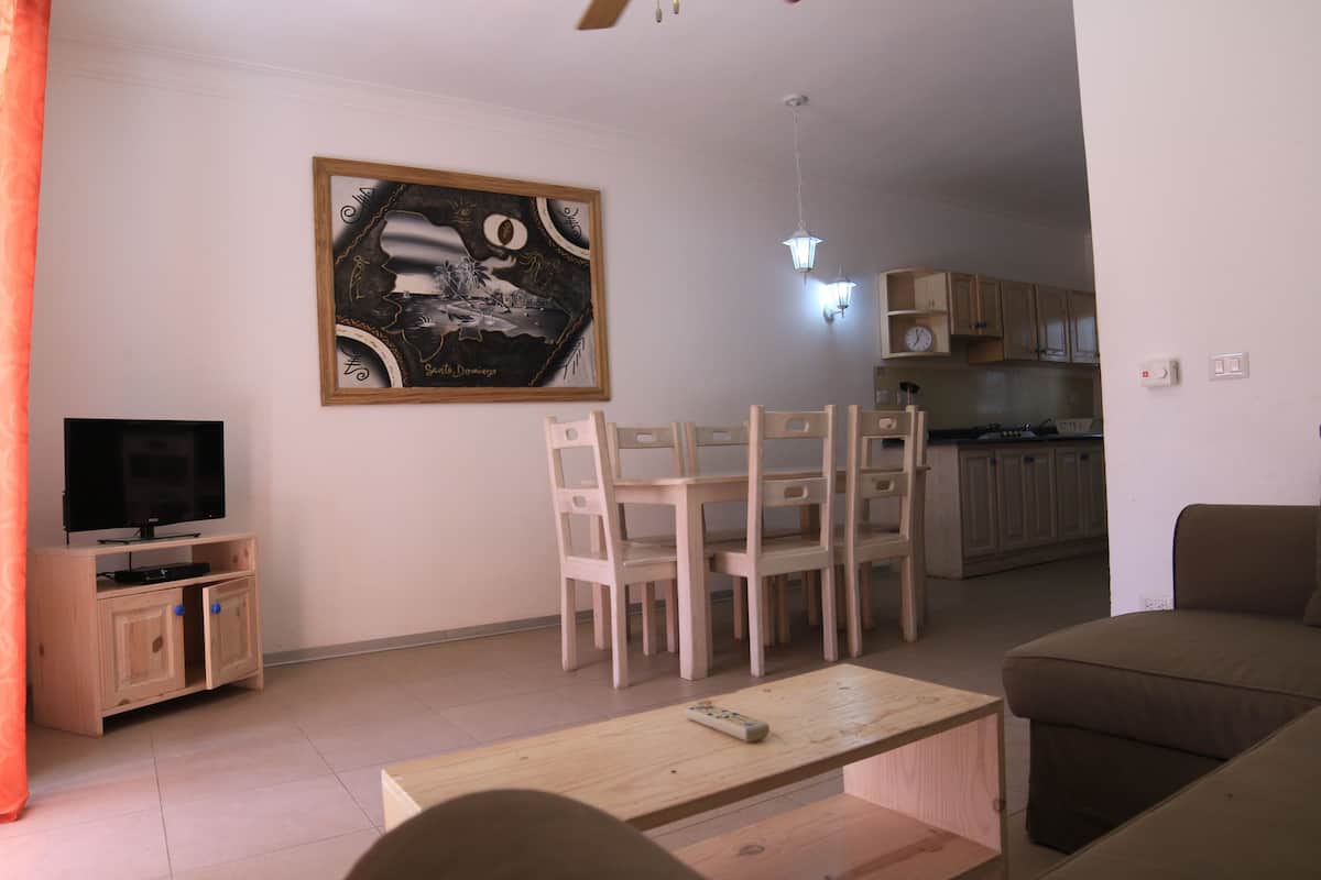 Ein Wohnzimmer mit Fernseher, Holzstühlen, einer Couch und einem Bild an der Wand.