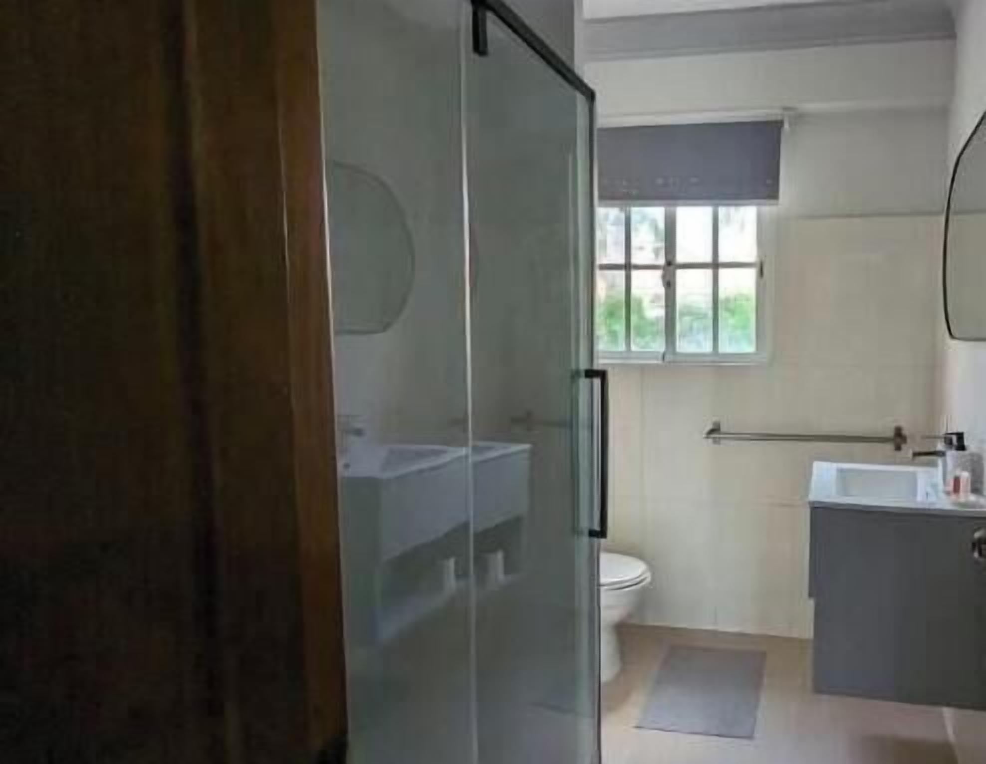 Un baño con puerta de vidrio, inodoro, lavabo y ventana.