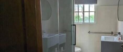 Un baño con puerta de vidrio, inodoro, lavabo y ventana.
