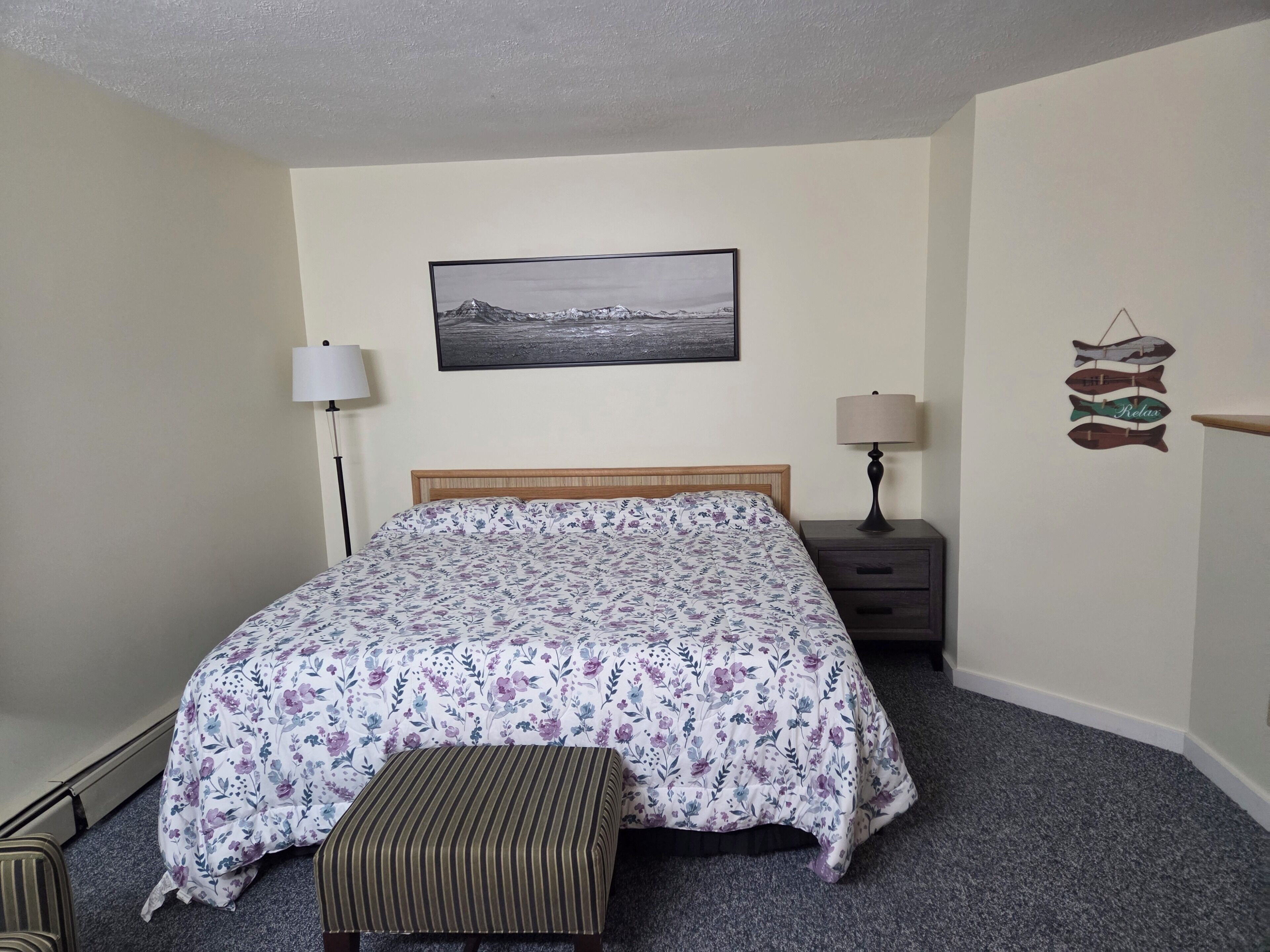 A bedroom with a bed, two bedside tables, a nightstand, a bench, a wall-mounted picture, and a wall decoration.