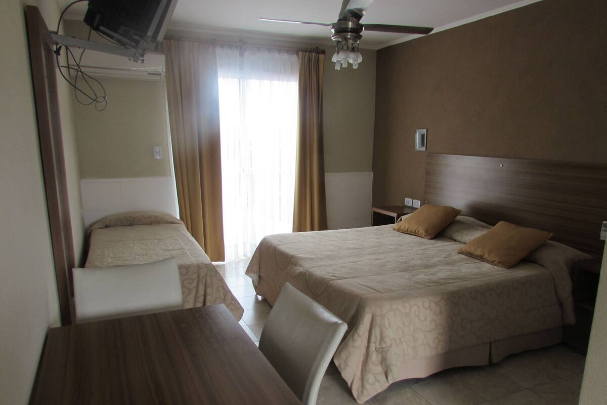 A hotel room with two beds, a desk, and a ceiling fan.