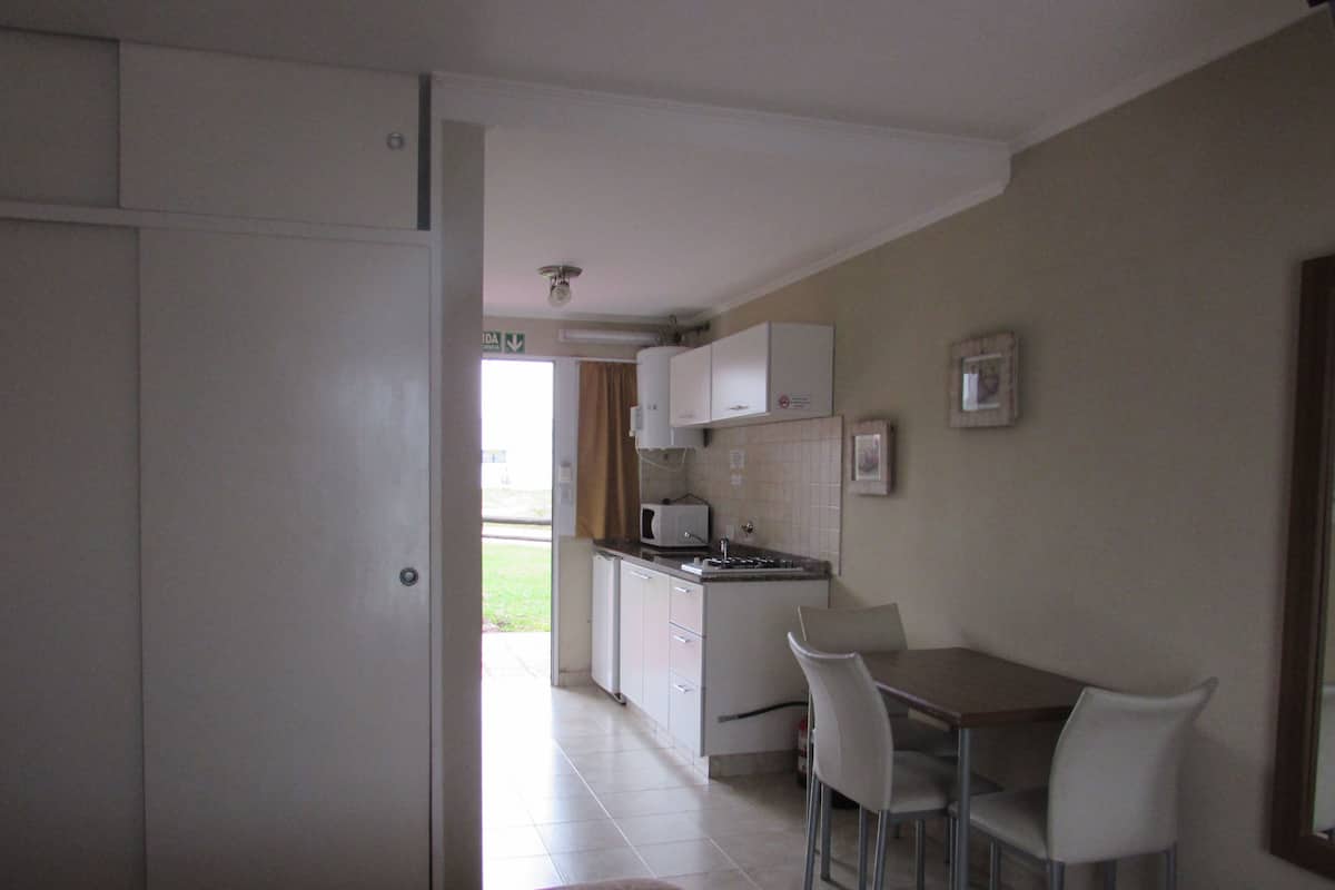 A compact kitchen with white cabinets, a microwave, and a dining area with two chairs.