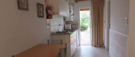 A compact kitchen with a dining table and chairs, a fire extinguisher, and a door leading outside.