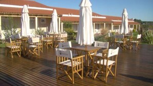 Une terrasse extérieure avec des meubles en bois et des parasols blancs, donnant sur un bâtiment doté d’un toit rouge.