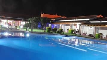 Una piscina con superficie de agua azul cristalina, rodeada de edificios de arquitectura tradicional e iluminación exterior.