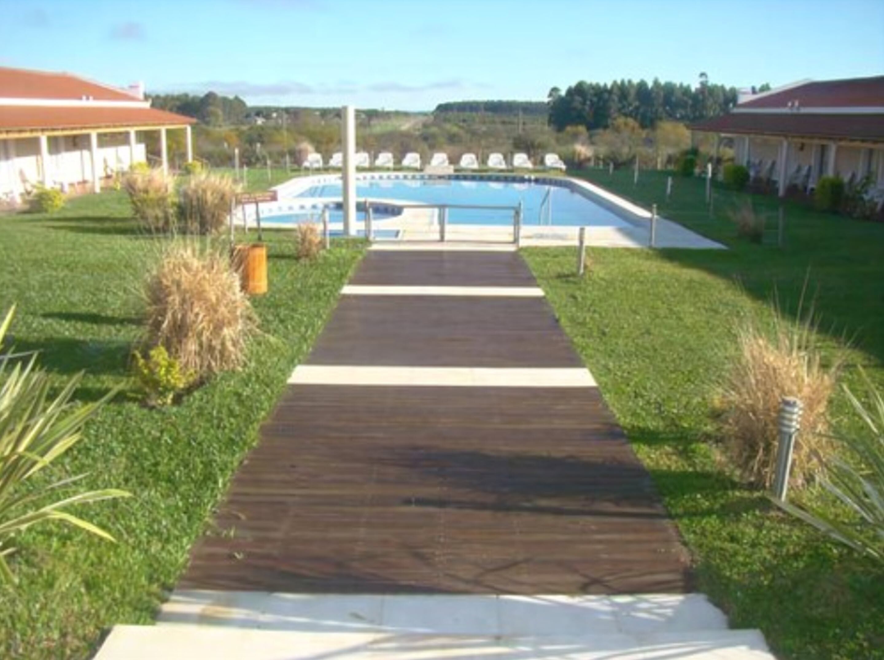 A wooden pathway leading to a swimming pool with lounge chairs and a covered area.