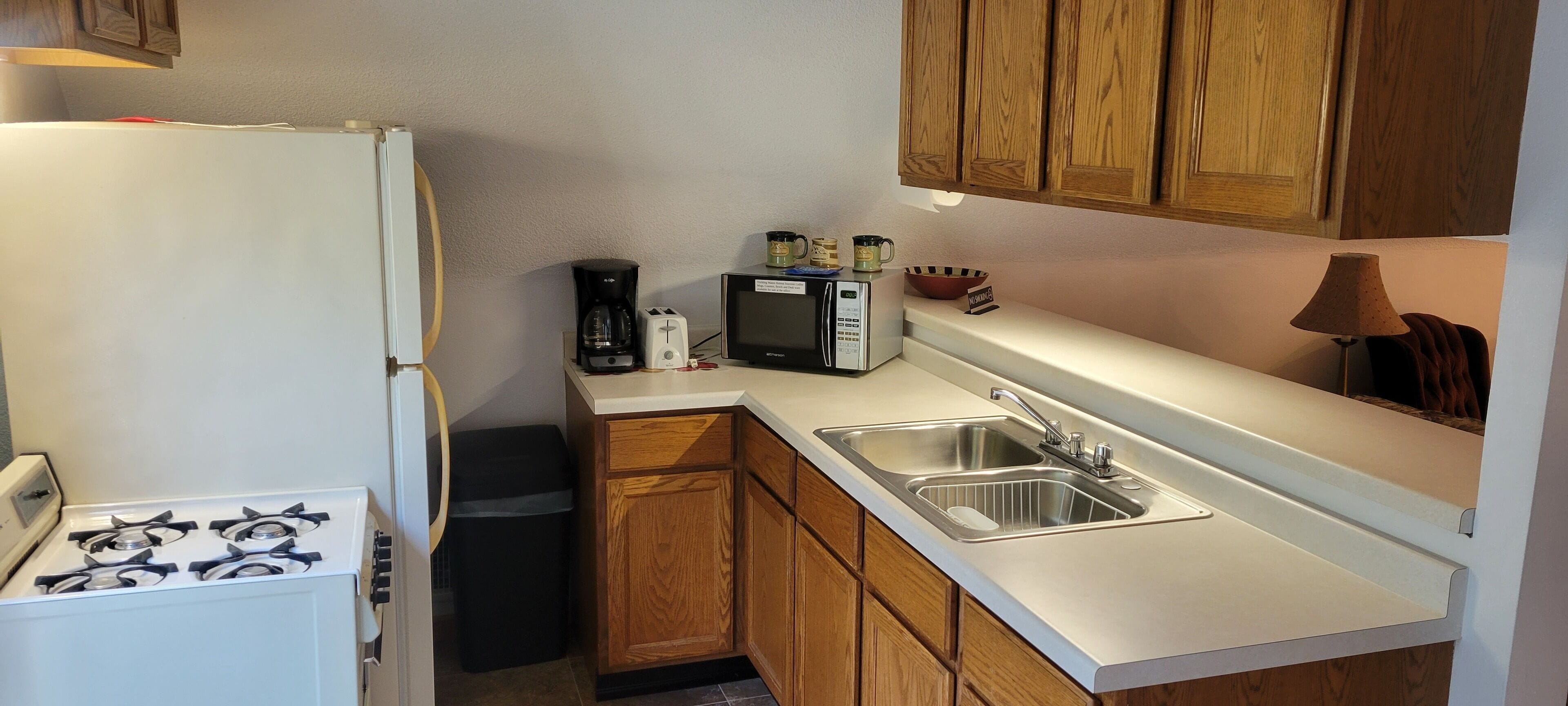 A compact kitchen with a stove, sink, microwave, and wooden cabinets.