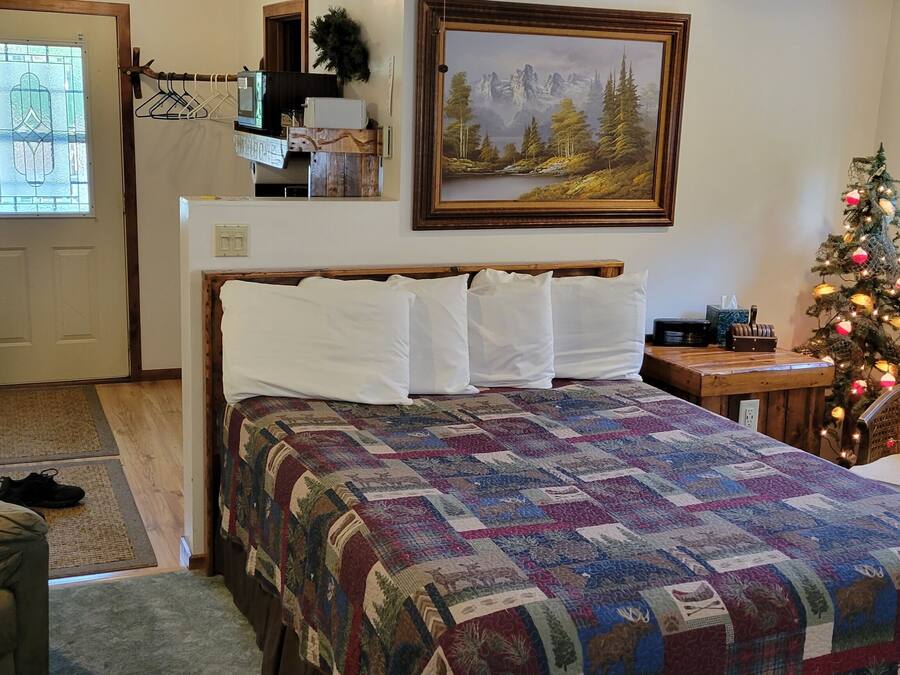 A bedroom with a bed, a chair, a Christmas tree, a painting, and a window with an air conditioner.