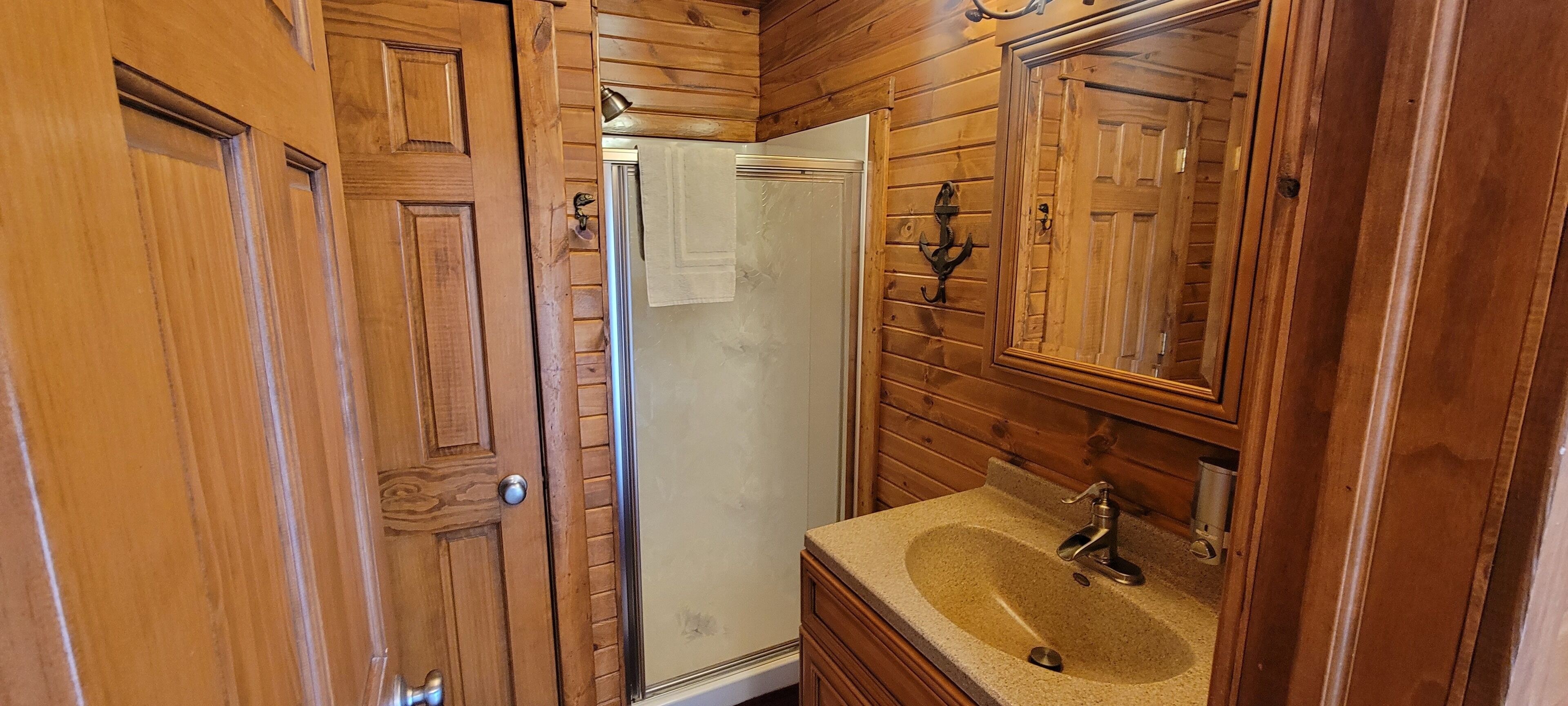 A wooden-paneled bathroom with a sink, mirror, and shower.