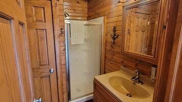 A wooden-paneled bathroom with a sink, mirror, and shower.