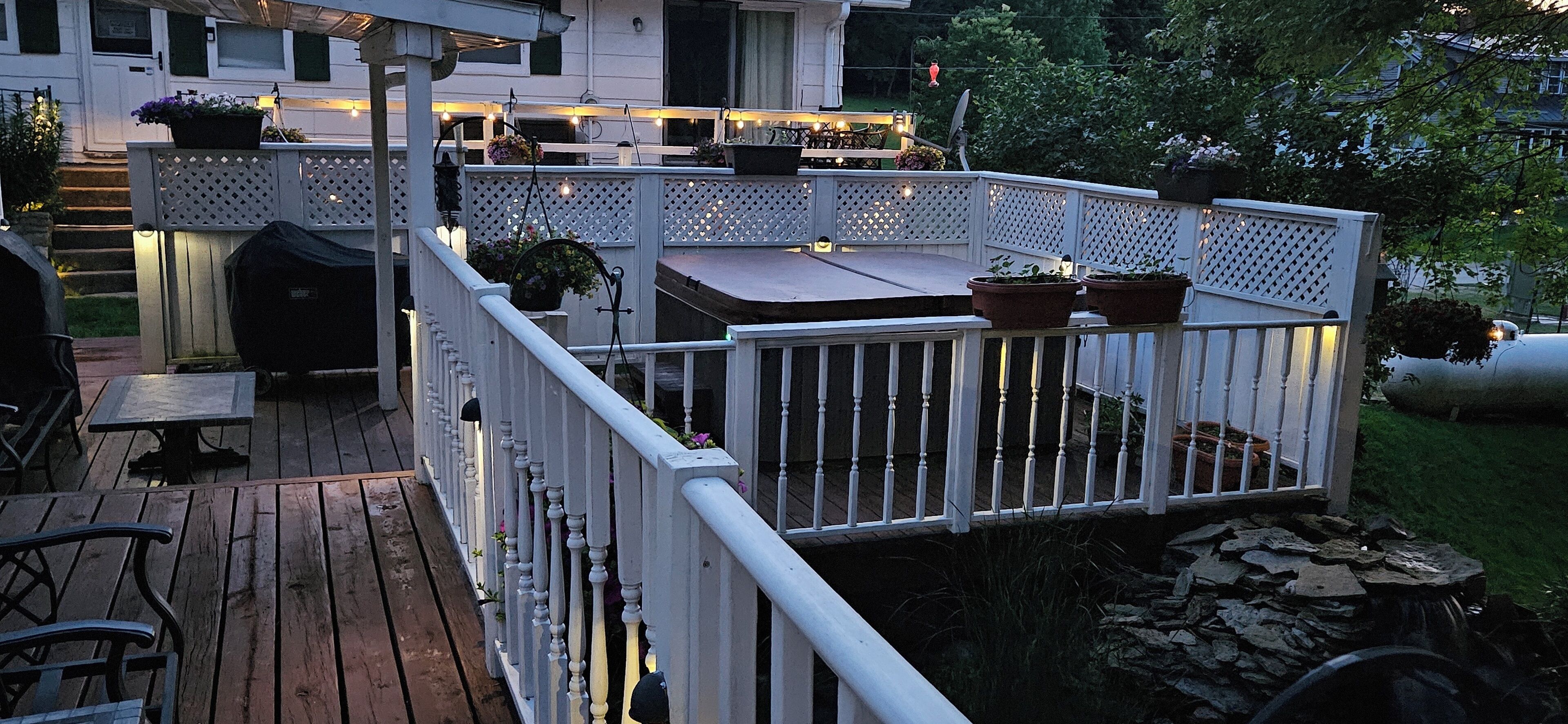 Une terrasse en bois avec une balustrade blanche, des plantes en pot et un barbecue.
