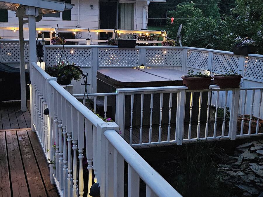 Une terrasse en bois avec une balustrade blanche, des plantes en pot et un barbecue.