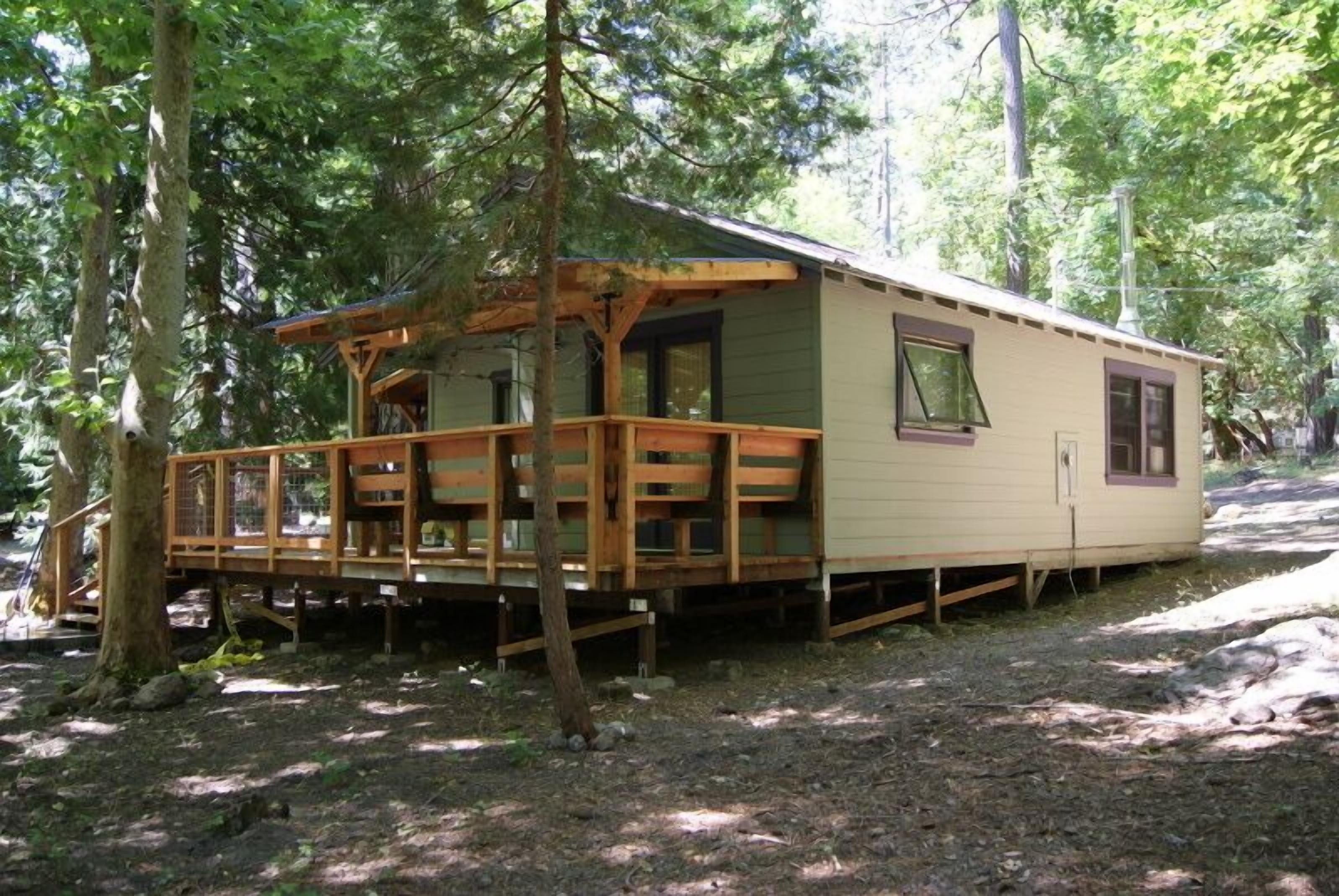 Uma cabana pequena com um deck de madeira e varanda coberta, cercada por árvores.
