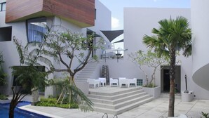 Une terrasse extérieure moderne avec une piscine, des meubles blancs et des palmiers.