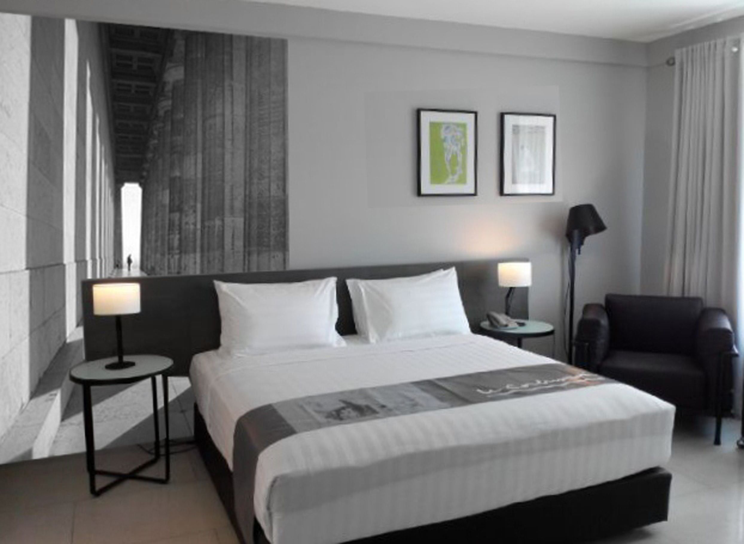 A modern hotel room with a large bed, two bedside tables, a chair, and artwork on the wall.
