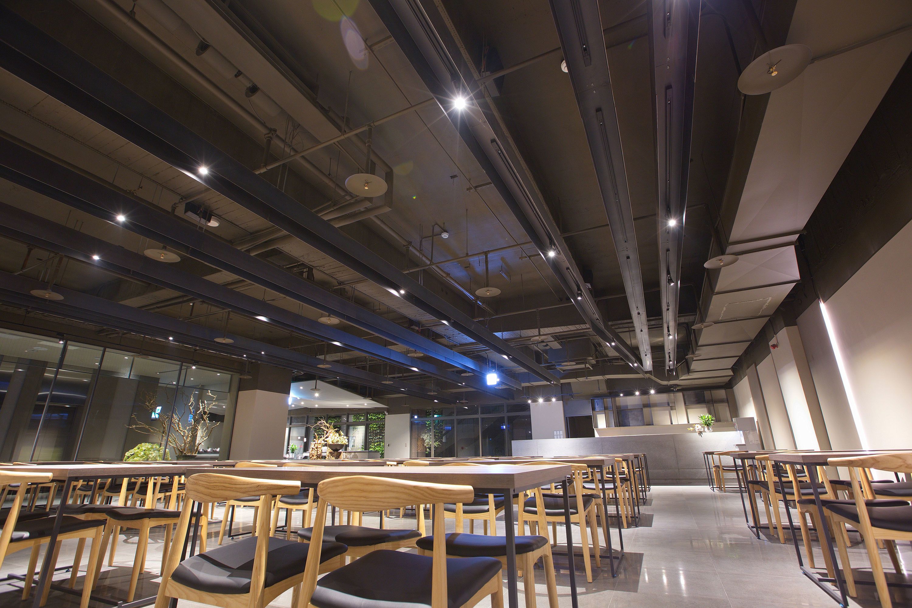 A modern dining area with wooden tables and chairs, a central counter, and large windows allowing natural light.