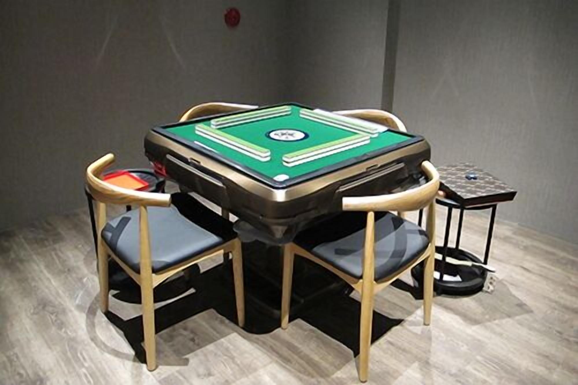 Una mesa de billar con superficie de fieltro verde, rodeada por cuatro sillas de madera con cojines negros.