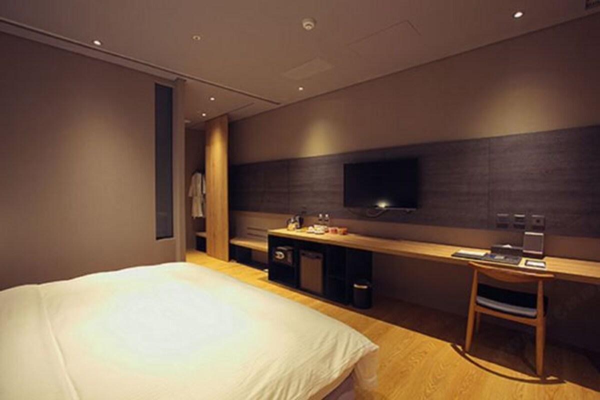 Quarto de hotel moderno com uma cama grande, uma escrivaninha com cadeira, televisão e uma pequena copa.