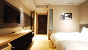 Una habitación de hotel moderna con un escritorio de madera, un televisor de pantalla plana grande, una cama con ropa blanca y dos cuadros en la pared.