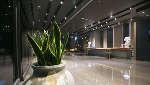 Un vestíbulo moderno con una recepción, una planta grande en maceta y un suelo pulido.