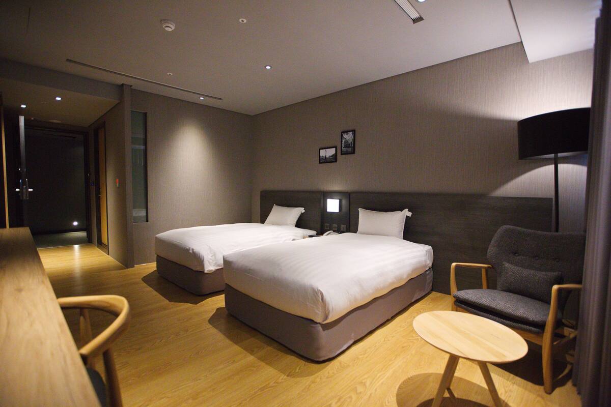 A hotel room with two beds, a desk, a chair, and a small table.