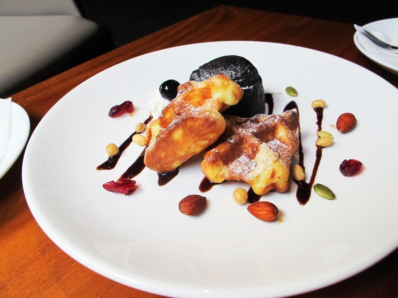 Une assiette de dessert comprenant une sphère de chocolat, deux parts de gâteau et divers fruits à coque et graines.