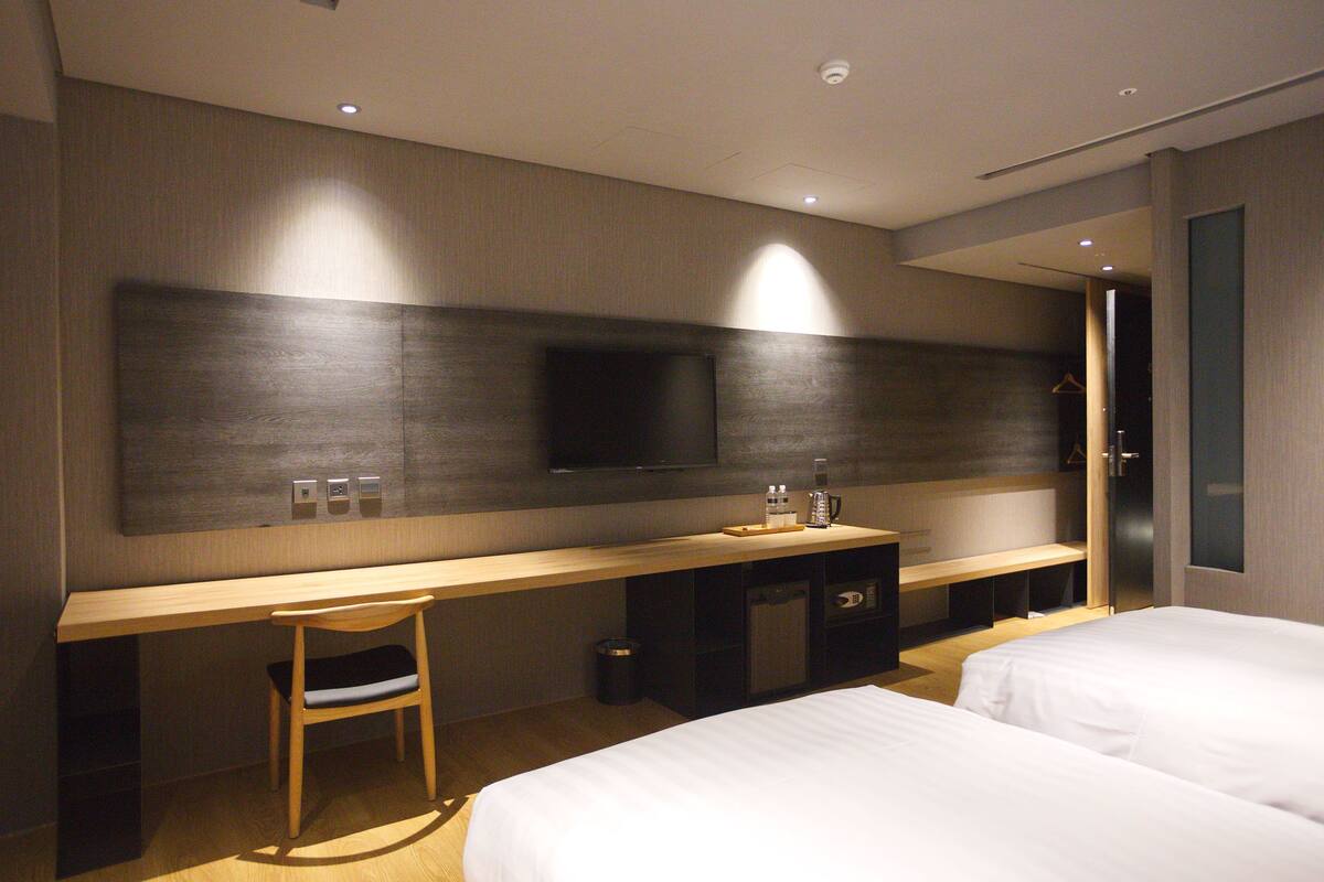 A modern hotel room with a wooden desk, a television, a bed, and a wardrobe.