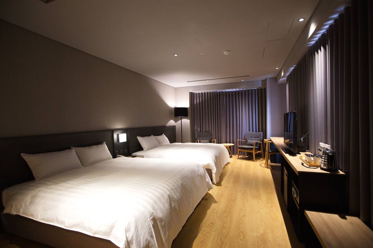 A hotel room with two beds, a desk with a computer, a chair, and a TV.