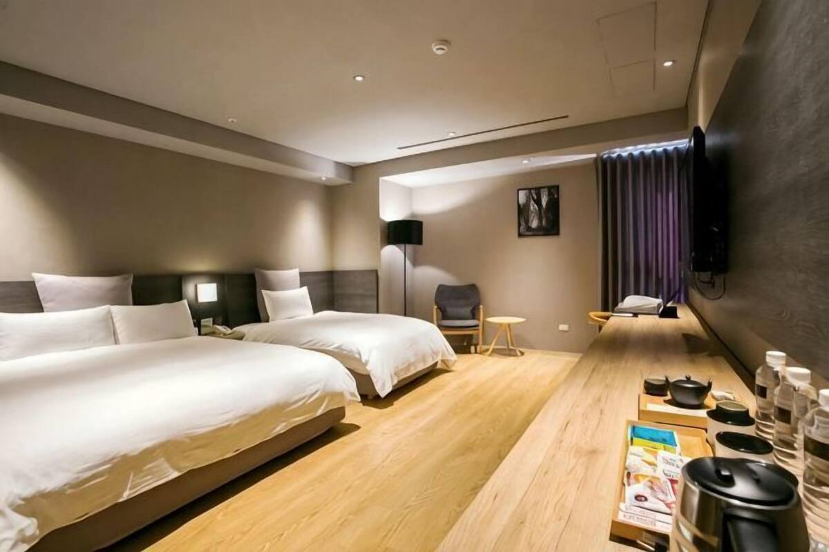 A hotel room with two beds, a wooden desk with amenities, a chair, and a TV mounted on the wall.