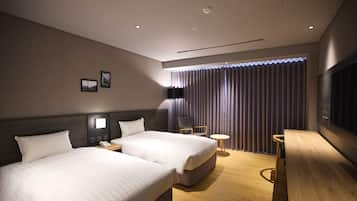 A hotel room with two beds, a desk, a chair, a small table, and a TV.