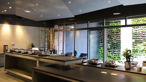 Un área de recepción moderna con una larga recepción, asientos y un gran ventanal con un panel verde.