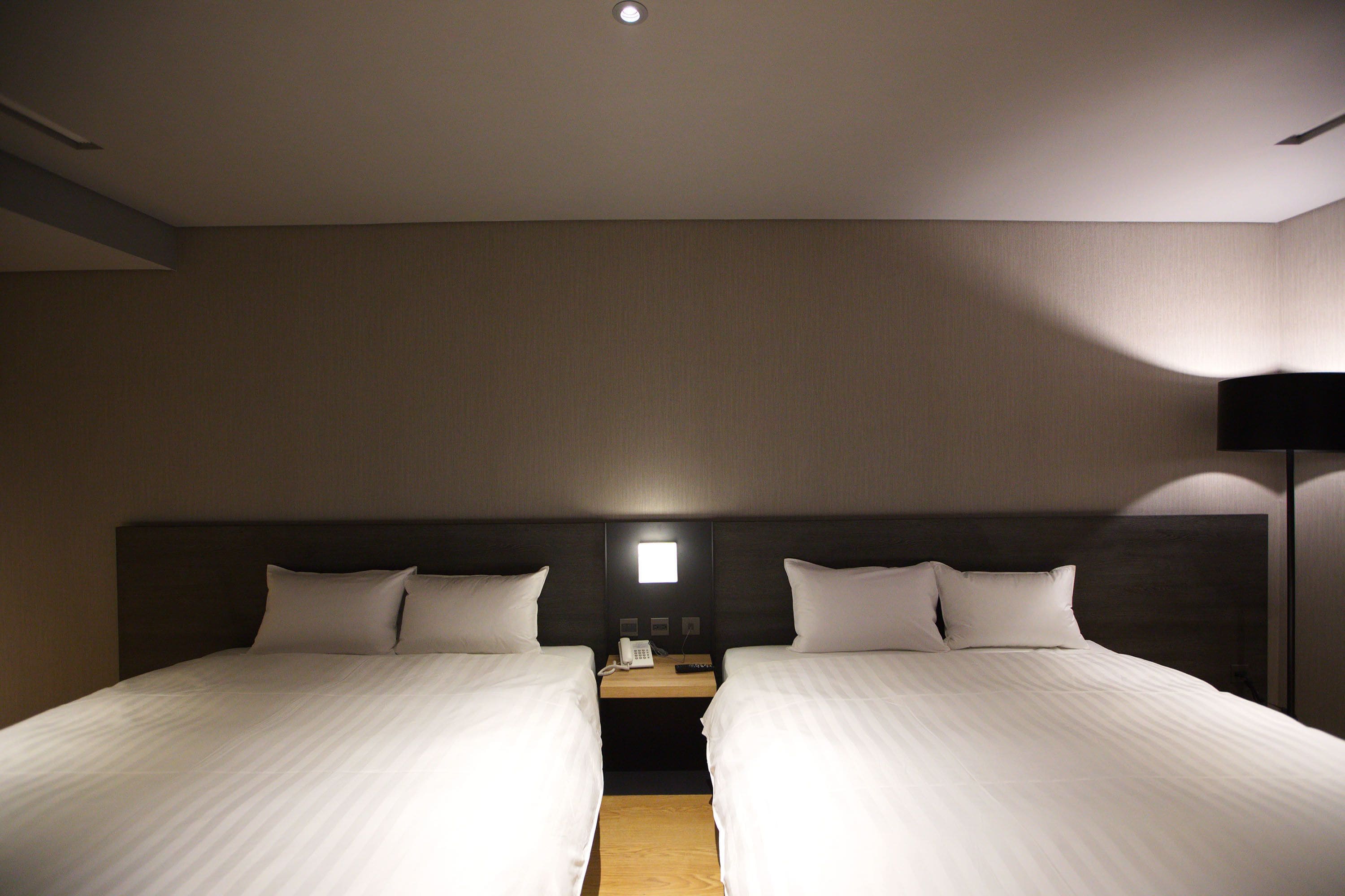 A hotel room with two single beds, a bedside table with a phone, and a lamp.