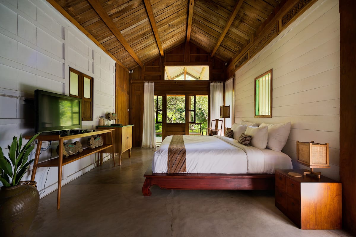 A spacious bedroom with a large bed, wooden ceiling, and a television on a wooden stand.