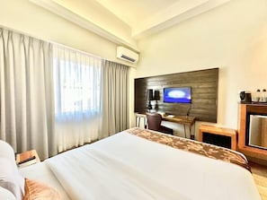 Habitació d'hotel amb un llit, un escriptori amb un ordinador, una televisió i un aparell d'aire condicionat.