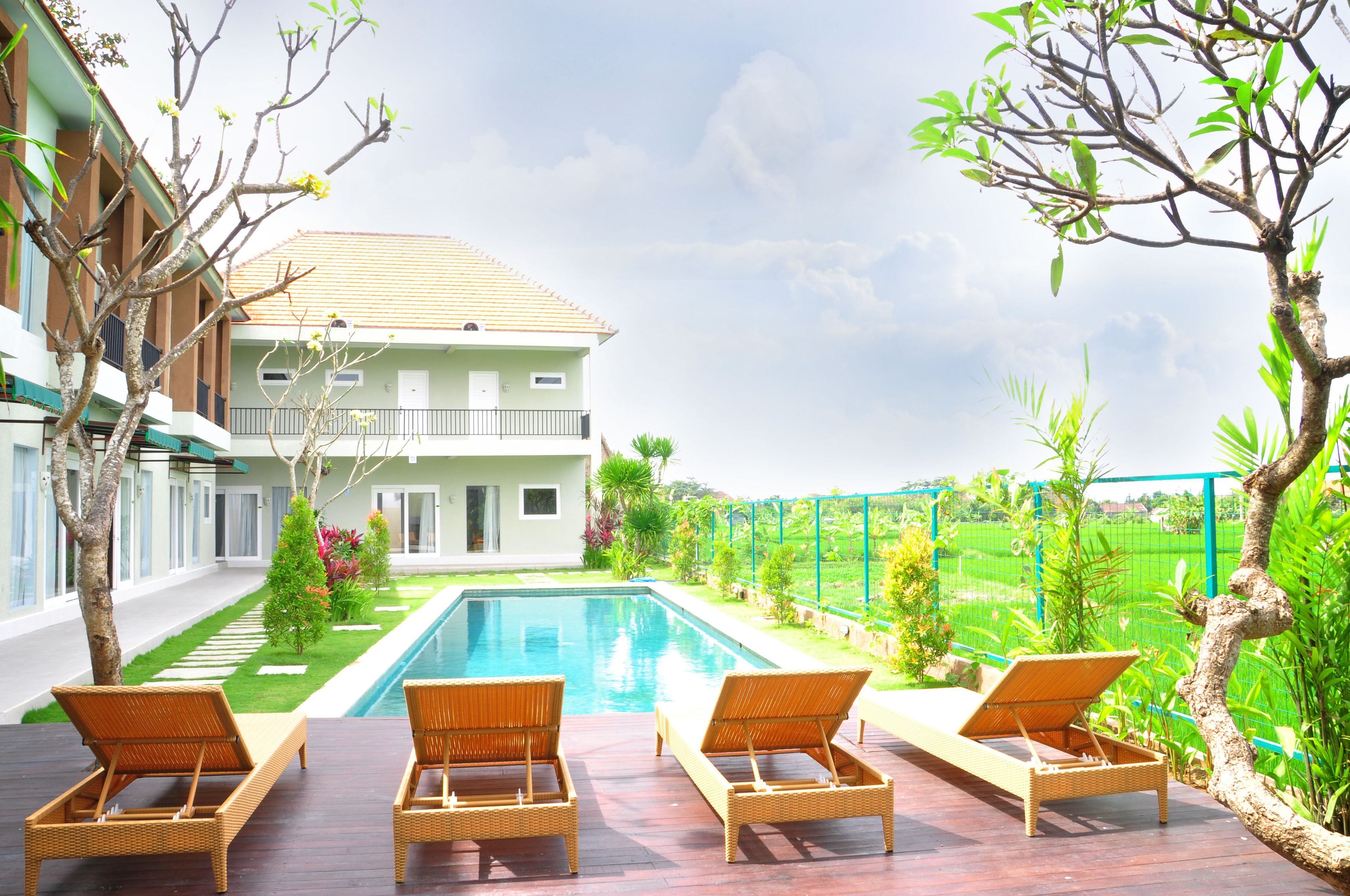 A poolside area with lounge chairs, a swimming pool, and a view of a house with a balcony.