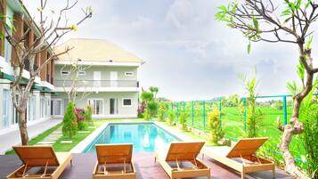 A poolside area with lounge chairs, a swimming pool, and a view of a house with a balcony.