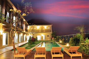 A hotel with a pool, lounge chairs, and a well-lit balcony. - Villa Tangtu Beach Inn (Denpasar)