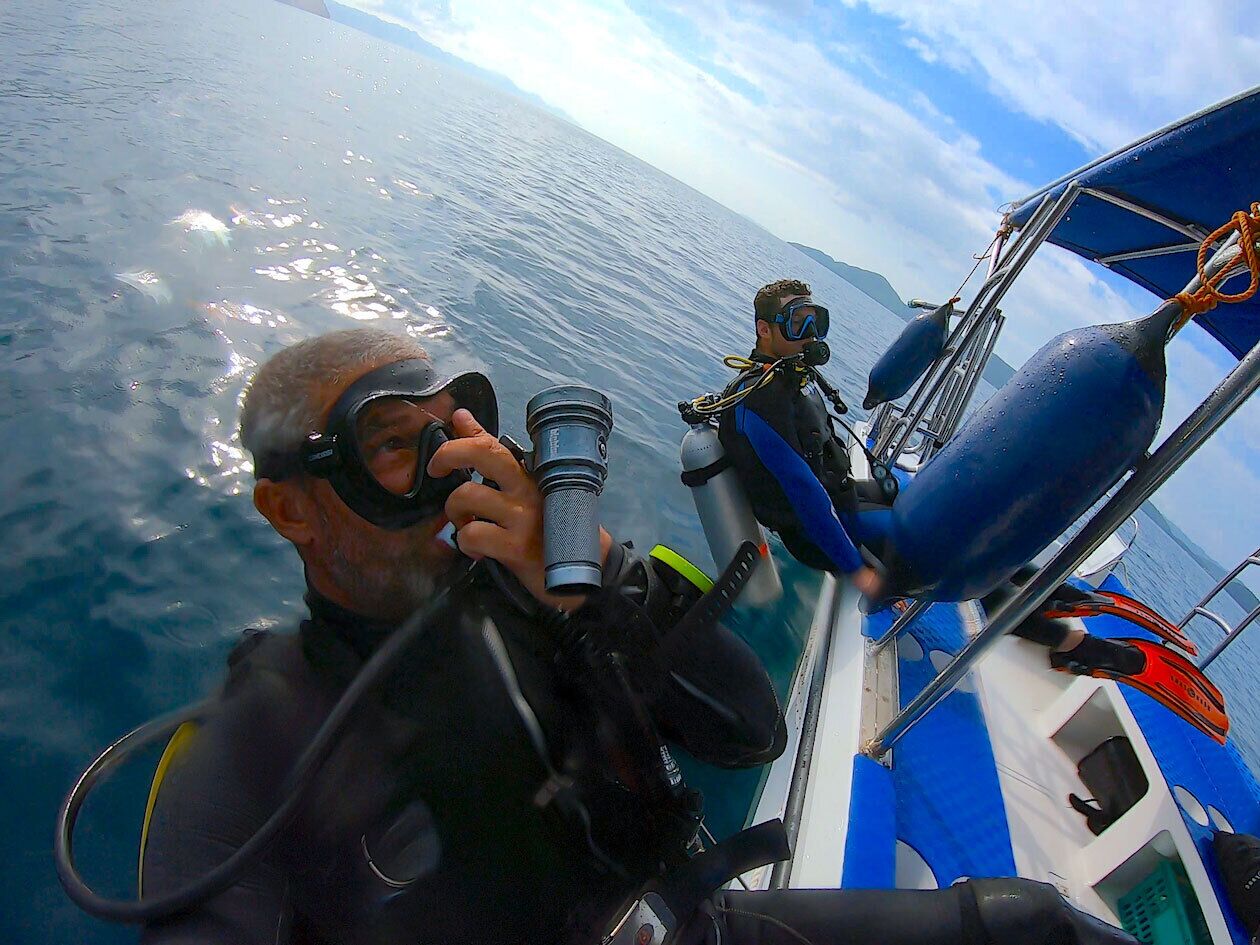 A diver with a camera on a boat, water visible around the boat.