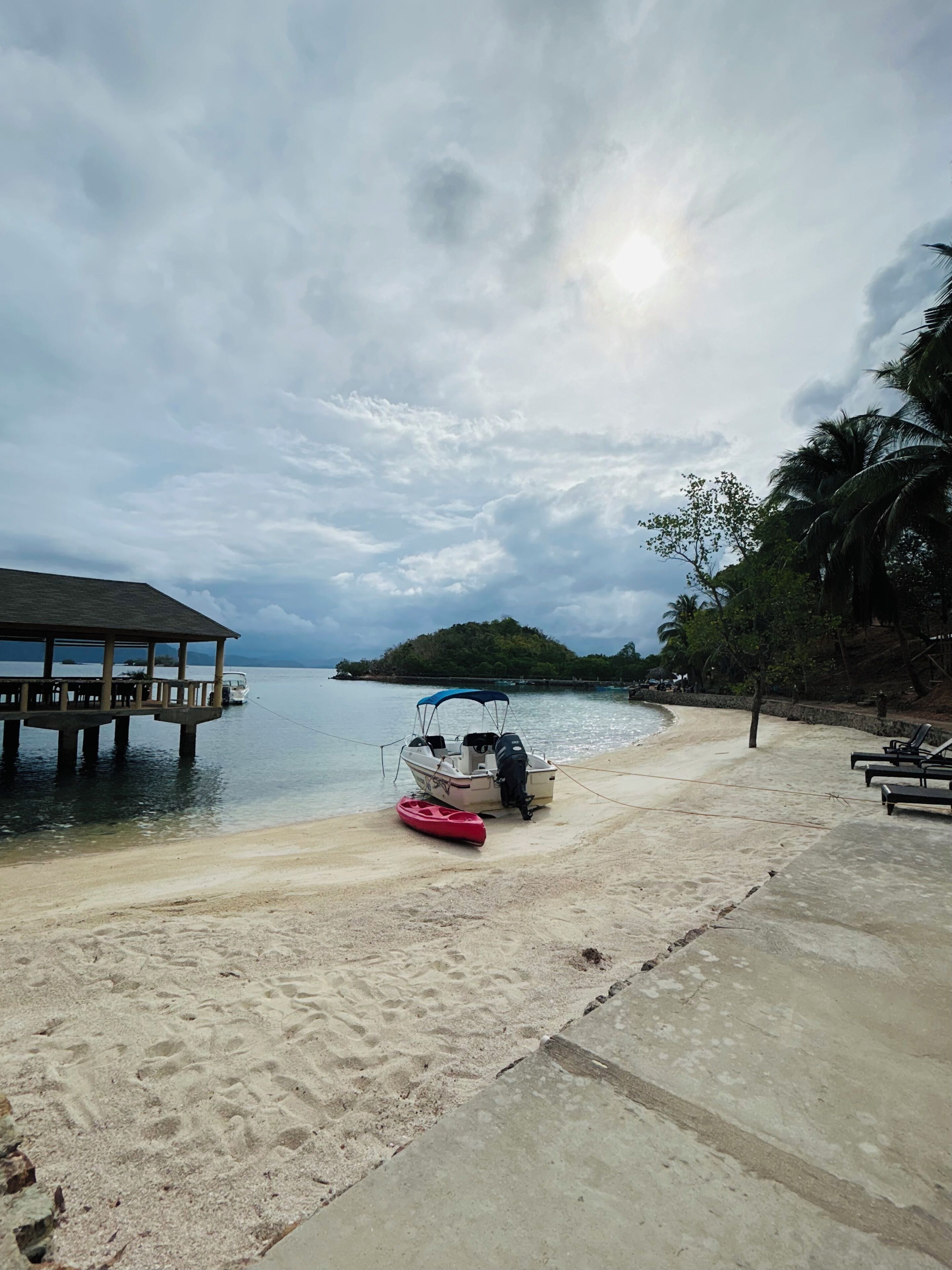 Une plage avec une promenade en béton, un petit bateau et un kayak rouge.