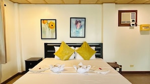 A hotel room with a large bed, two paintings on the wall, a bedside table, and a wall-mounted air conditioning unit.