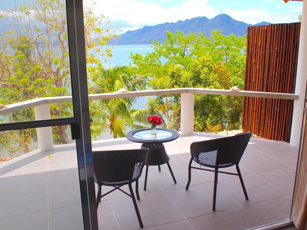 A balcony with two chairs and a table, overlooking a body of water and greenery. - Chindonan Dive and Beach Resort (Coron)