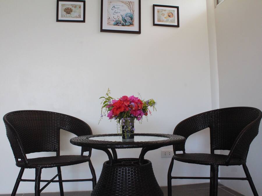 A round table with two wicker chairs, a vase with flowers, and three framed pictures on the wall.