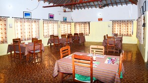 A dining area with multiple tables and chairs, a patterned floor, and a corrugated metal roof. - Nepal Wildlife Resort (Thakudwara)