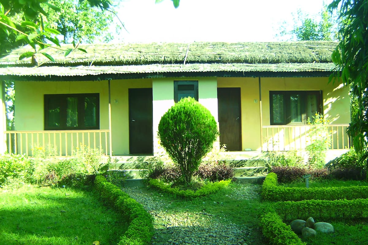 Um edifício de dois andares com telhado de palha, um pequeno alpendre e um jardim bem cuidado com um caminho de cascalho.