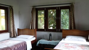 A room with two single beds, a small table with a bottle and glasses, and a window with curtains. - Nepal Wildlife Resort (Thakudwara)