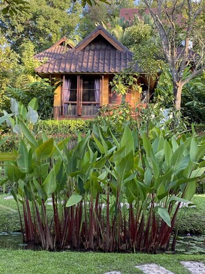 A house with a tiled roof and wooden windows, surrounded by lush greenery and a pond.