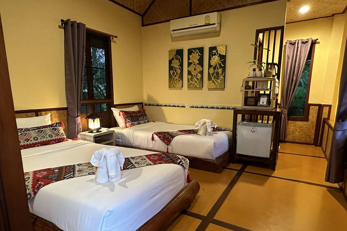Una habitación de hotel con dos camas, una mesita con una lámpara, un equipo de aire acondicionado y una ventana con cortinas.