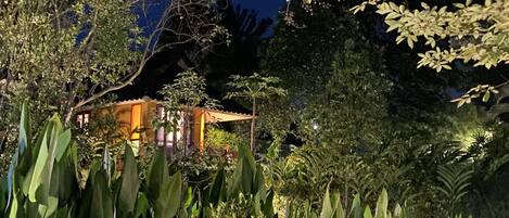 A secluded villa surrounded by dense foliage, with a visible structure featuring a curved roof and a small porch.