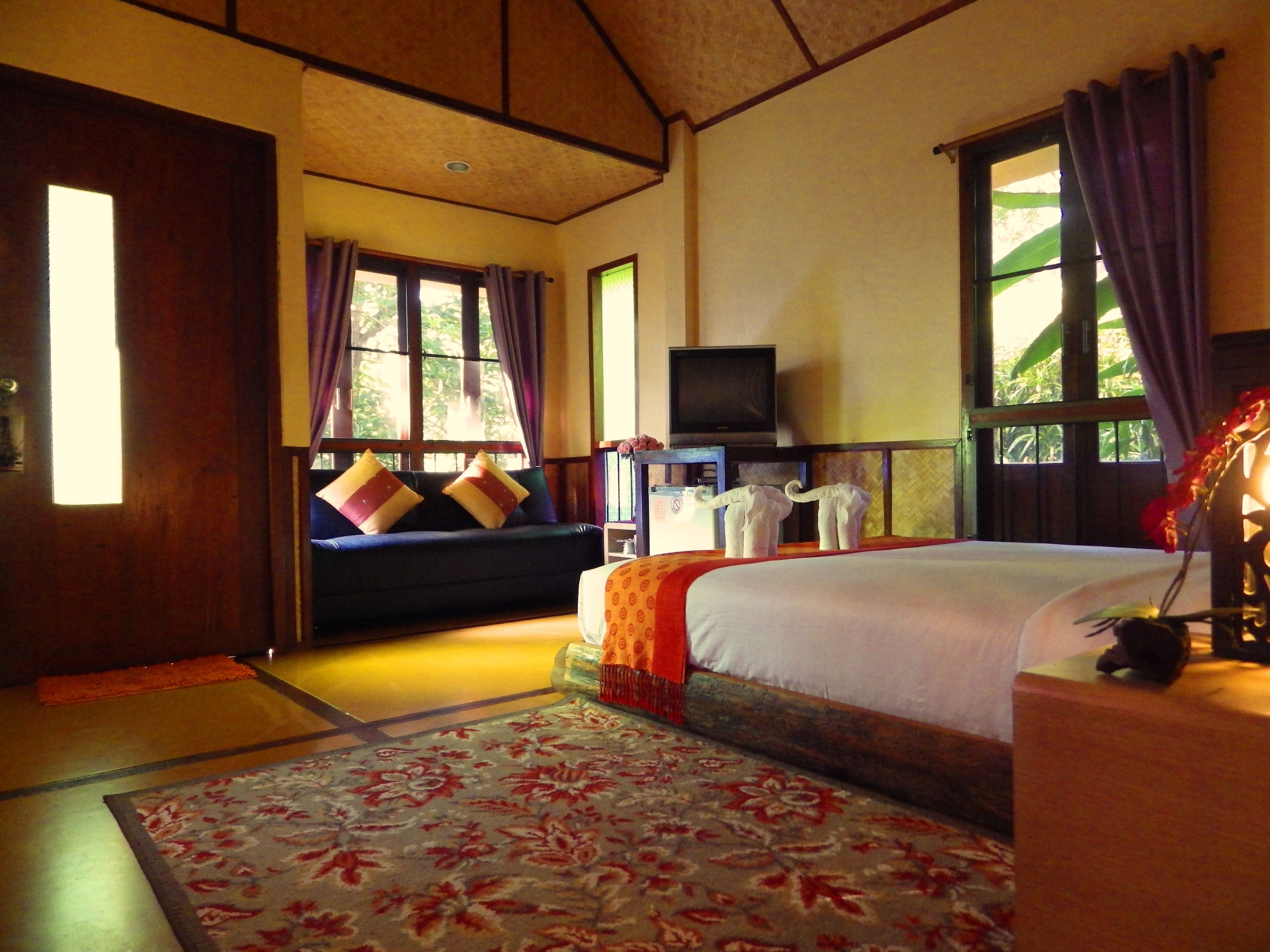 A room with a bed, a sofa, a television, and a window with curtains.