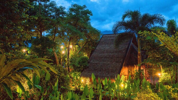 A thatched-roof structure surrounded by lush greenery and illuminated by ambient lighting. - PuraVida Pai Resort (Pai)